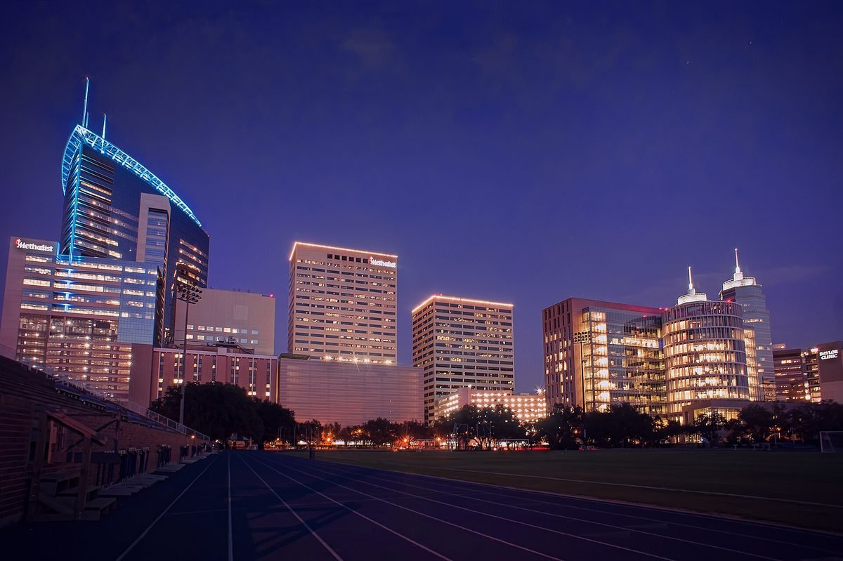 The Texas Medical Center towers in Houston lit at dusk, seen across an empty running track