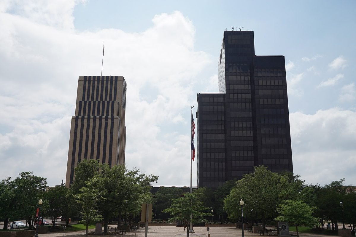 Two office towers rising above a tree-lined plaza in downtown Tyler